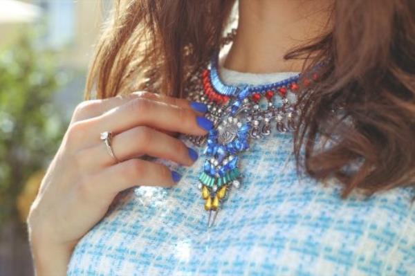 Brown-haired girl in a blue dress with a necklace. Large necklace rhinestones. Thin hand with blue nail. Fashion trends. Street fashion. Trendy, stylish. Fashio<em></em>nable girl.